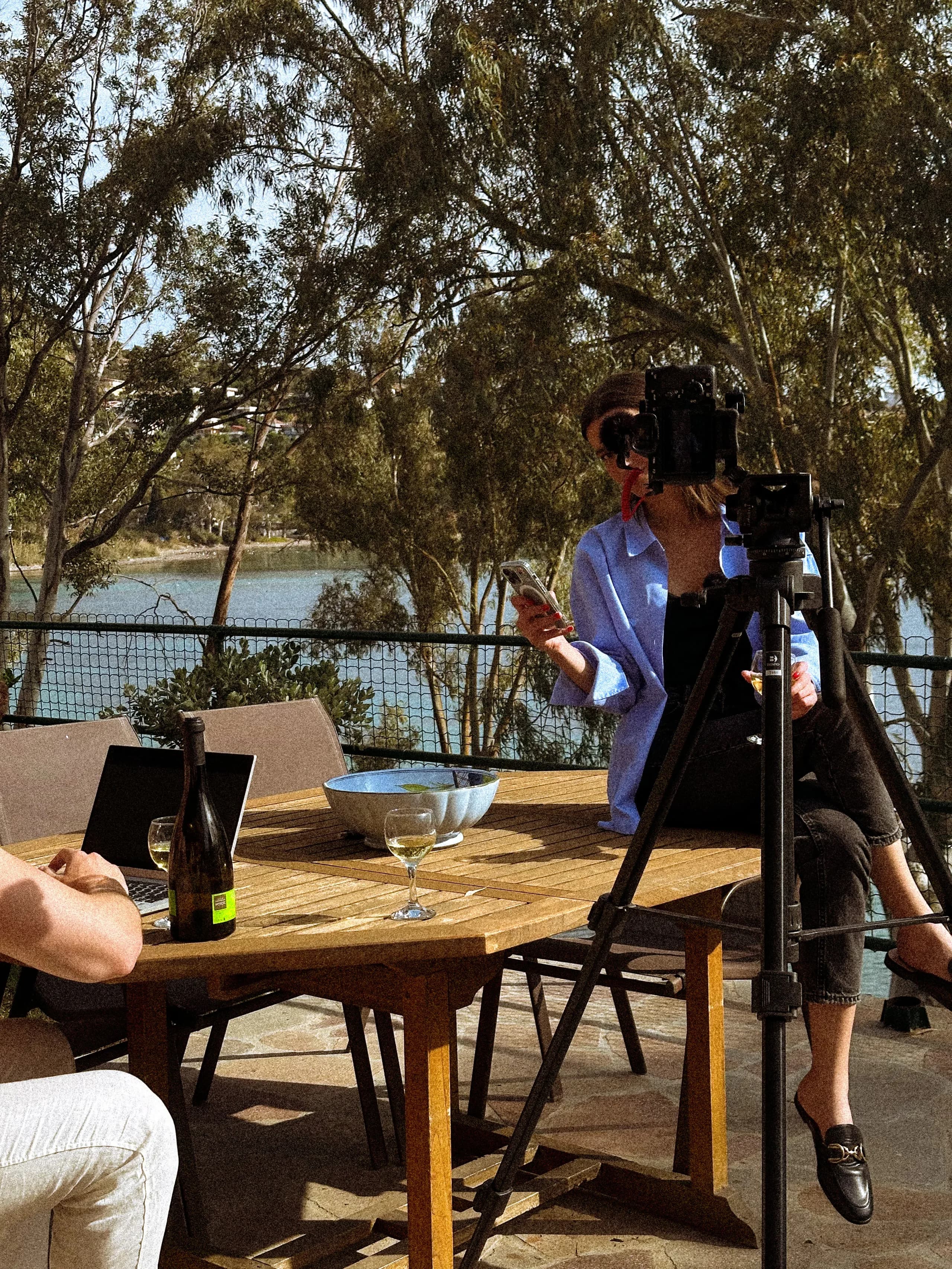 Videographer filming a table setup outdoors beside the water