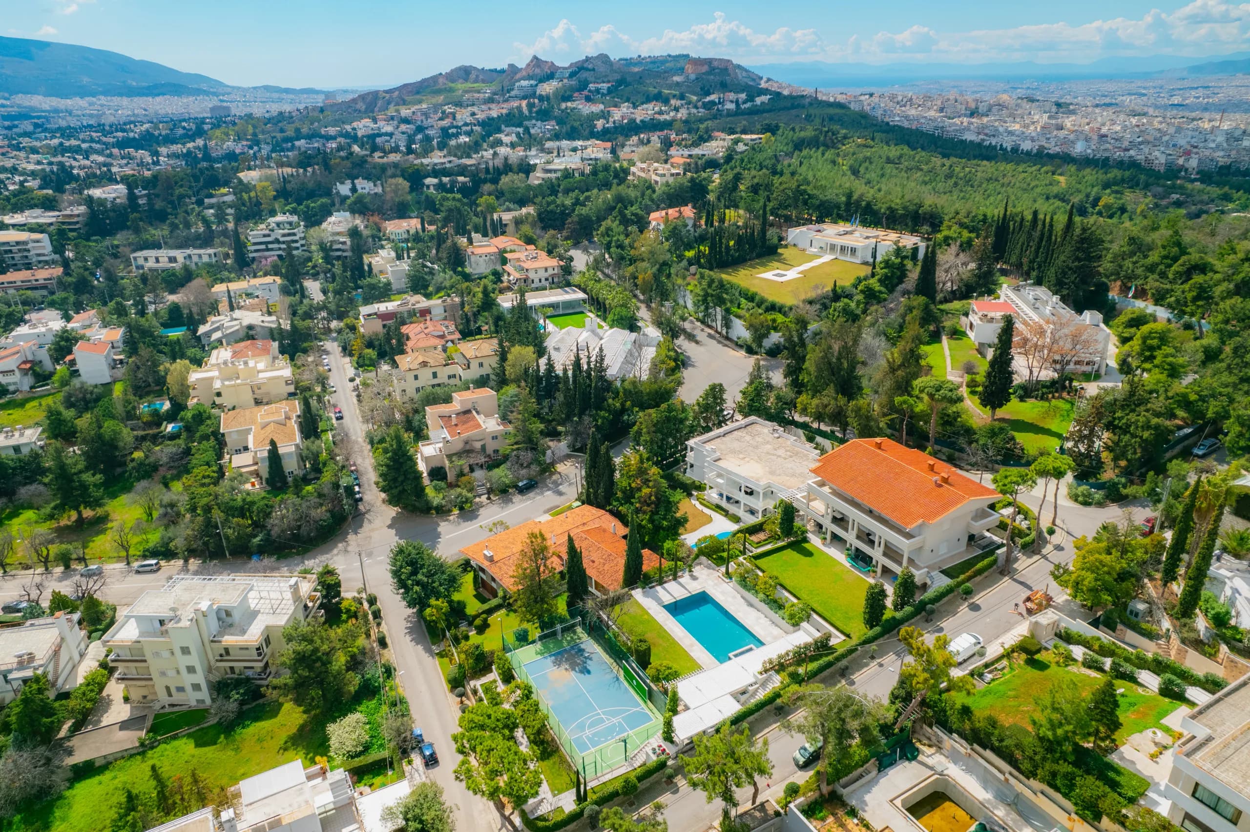 Aerial view of a residential neighbourhood in Greece with houses, pools and tree lined streets