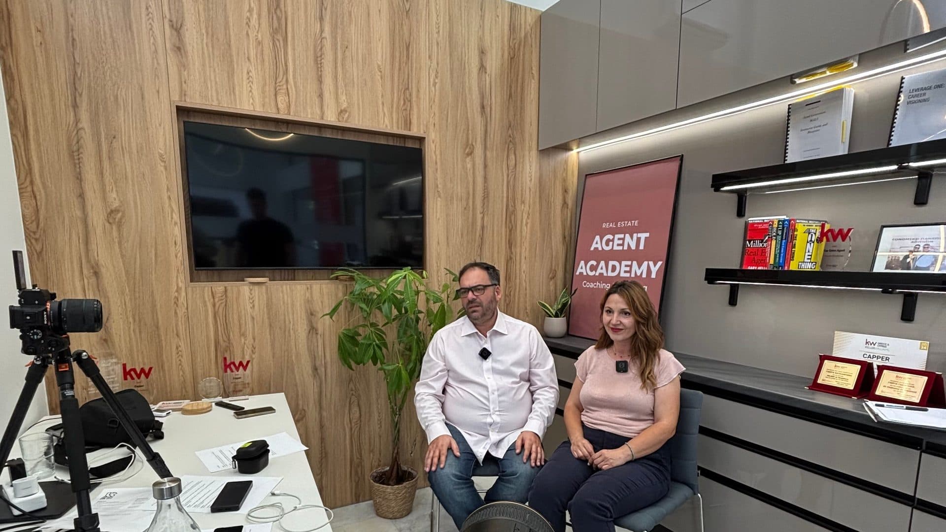 Δύο σύμβουλοι της Keller Williams μπροστά σε κάμερα και τρίποδο, σε γύρισμα μέσα στο γραφείο τους στην Αθήνα